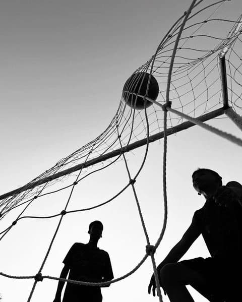 Silhouettes of two young athletes by a volleyball net against the sky